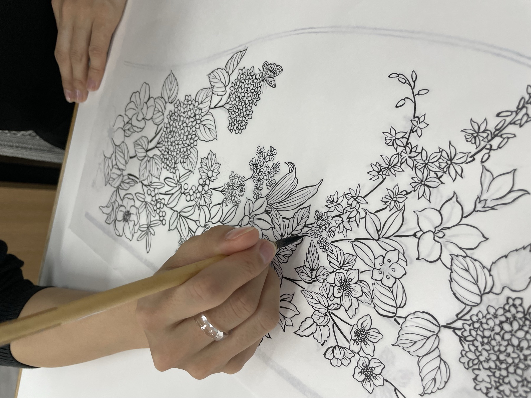 筆を持つ手元と、繊細な花の下絵